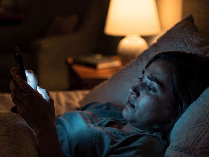 A woman lying in bed, lit by her phone screen